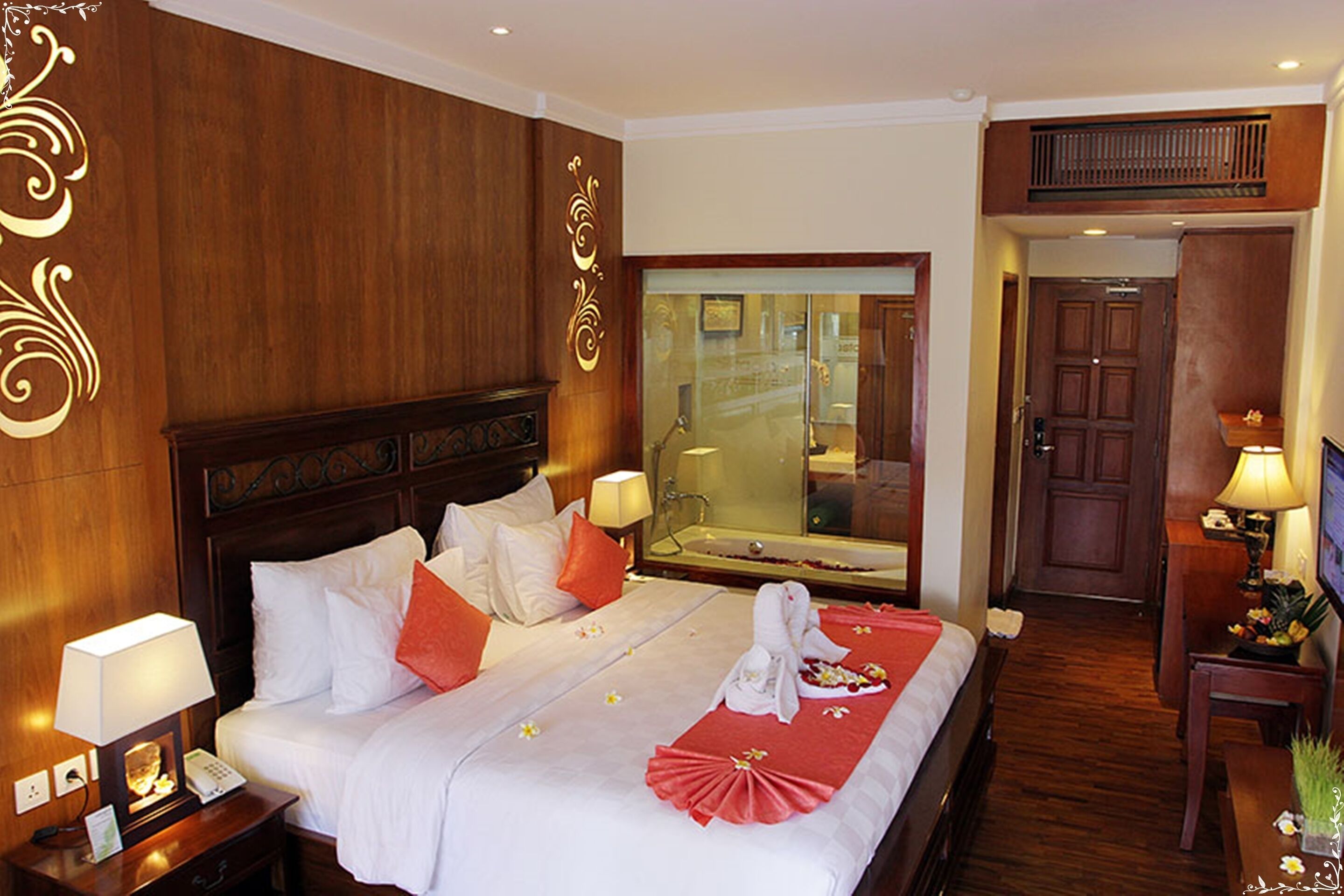 Une chambre d’hôtel avec un grand lit, une table de chevet avec une lampe, une tête de lit en bois, un miroir et une porte.