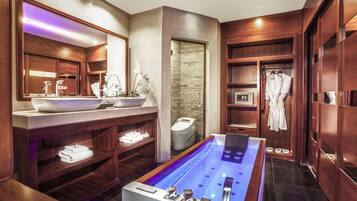 A modern bathroom with a large bathtub, wooden shelving, a vanity with a large mirror, and a stone wall.