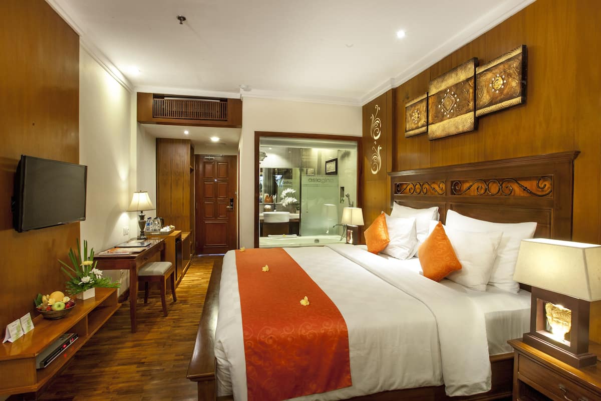 A hotel room with a bed, bedside table, lamp, and a television on the wall.