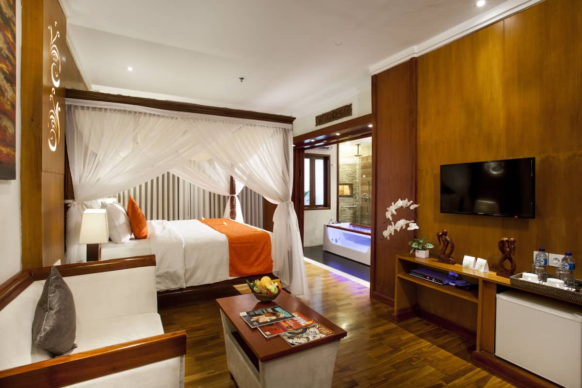 A hotel room with a bed, a sitting area with a coffee table, a TV, and a bathroom with a bathtub.
