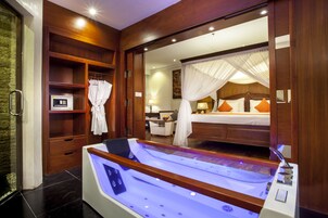 Una habitación de hotel moderna con una bañera grande, estanterías de madera, una cama con almohadas naranjas y un espejo que refleja la habitación.