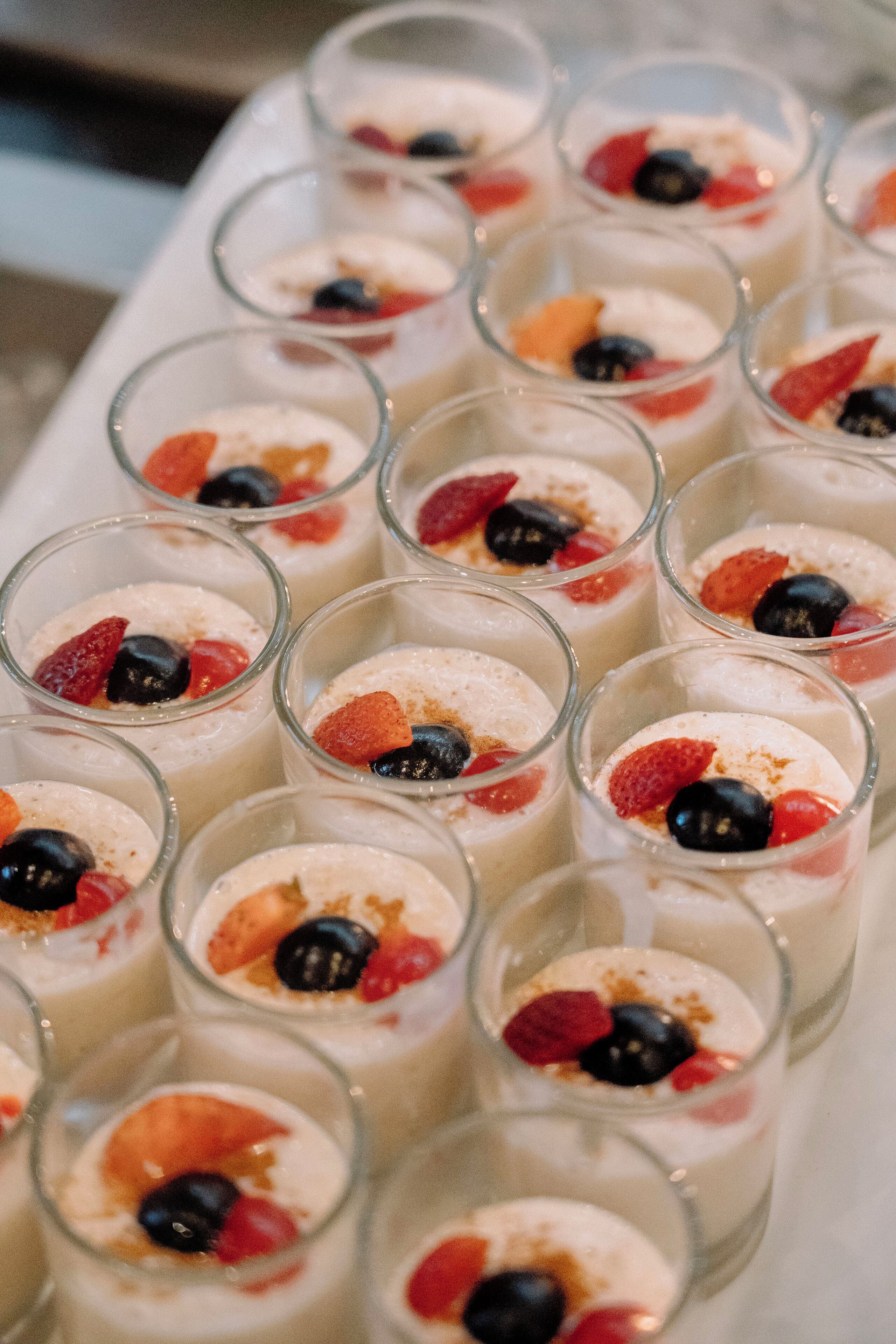 Een dienblad met dessertbekers, met een romige basis, belegd met verschillende soorten fruit en een strooiing van een bruinachtige substantie.