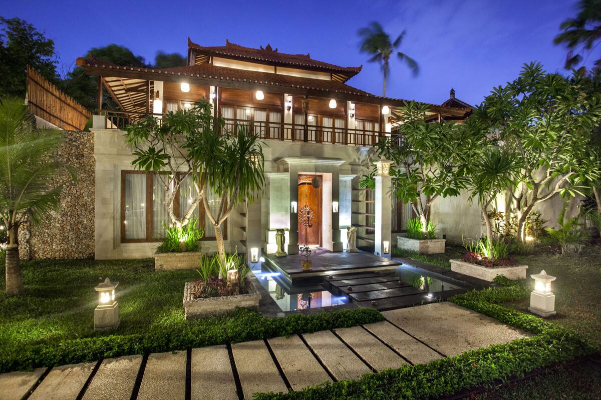 A traditional-style building with a water feature in front, surrounded by lush greenery and well-lit by ambient lighting.