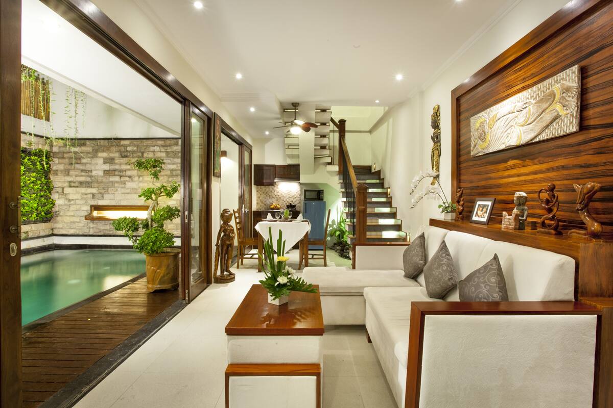 A modern living room with a pool, wooden flooring, and a staircase leading to an upper level.