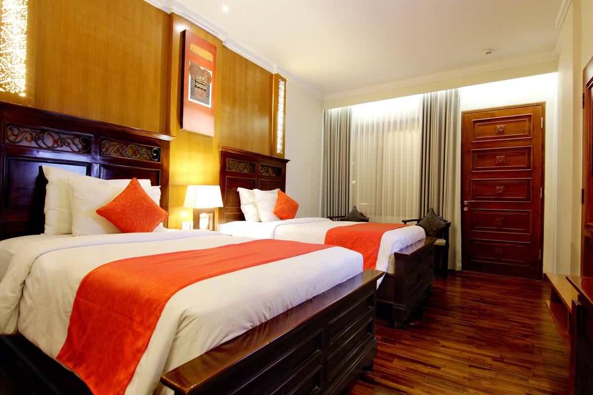A hotel room with two beds, wooden headboards, and a large wooden dresser.