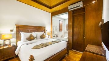 A hotel room with a wooden bed, a nightstand, a bedside lamp, a mirror, and a wooden bench.