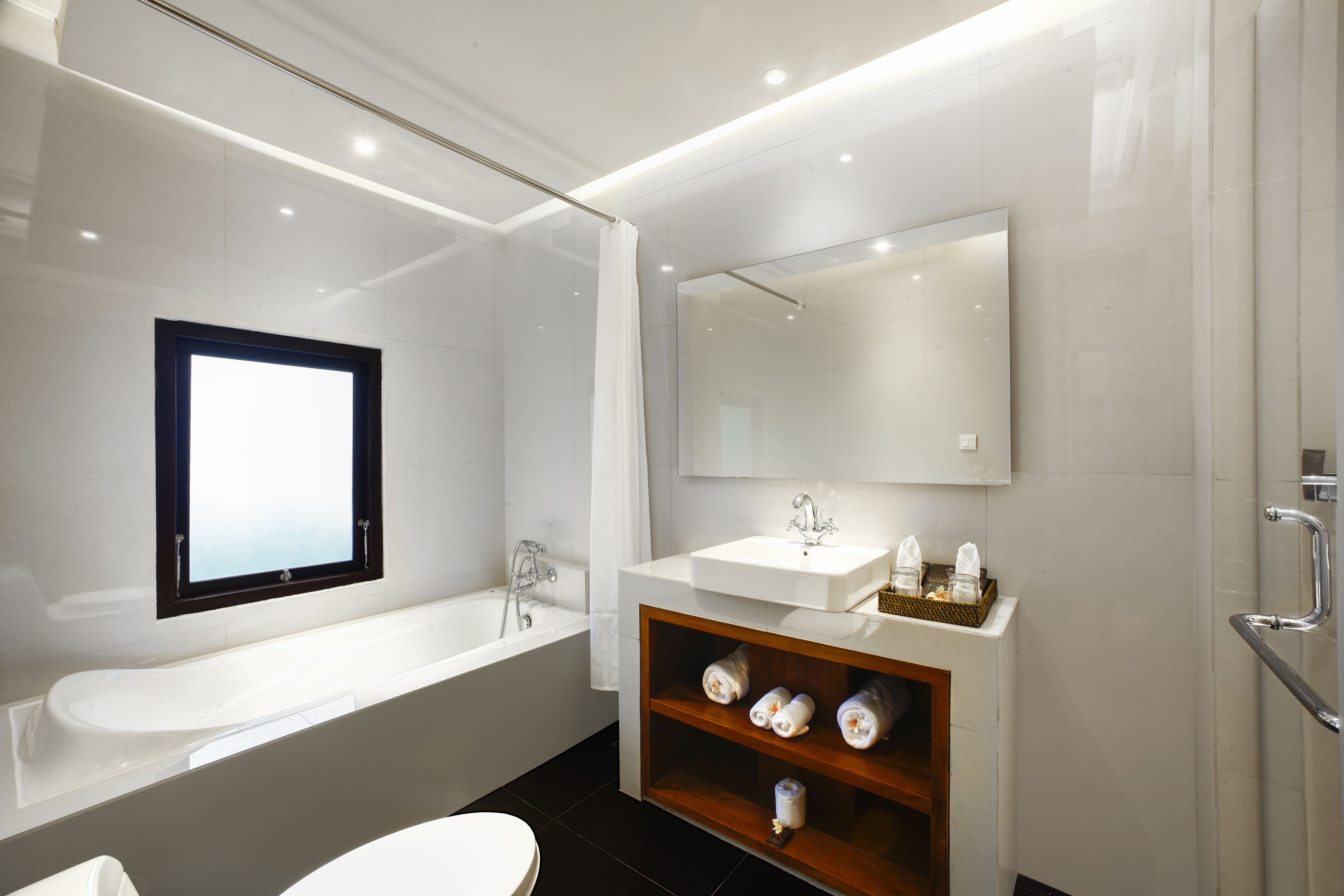 Un bany modern amb un lavabo blanc, un mirall gran, una banyera i una estant amb tovalloles.