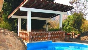 A swimming pool with a white pergola and a brick wall.
