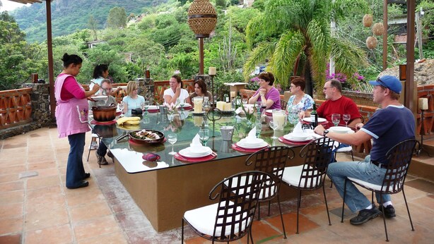 An outdoor dining area with a bamboo pergola, a central island with a glass top, and a scenic mountainous backdrop.