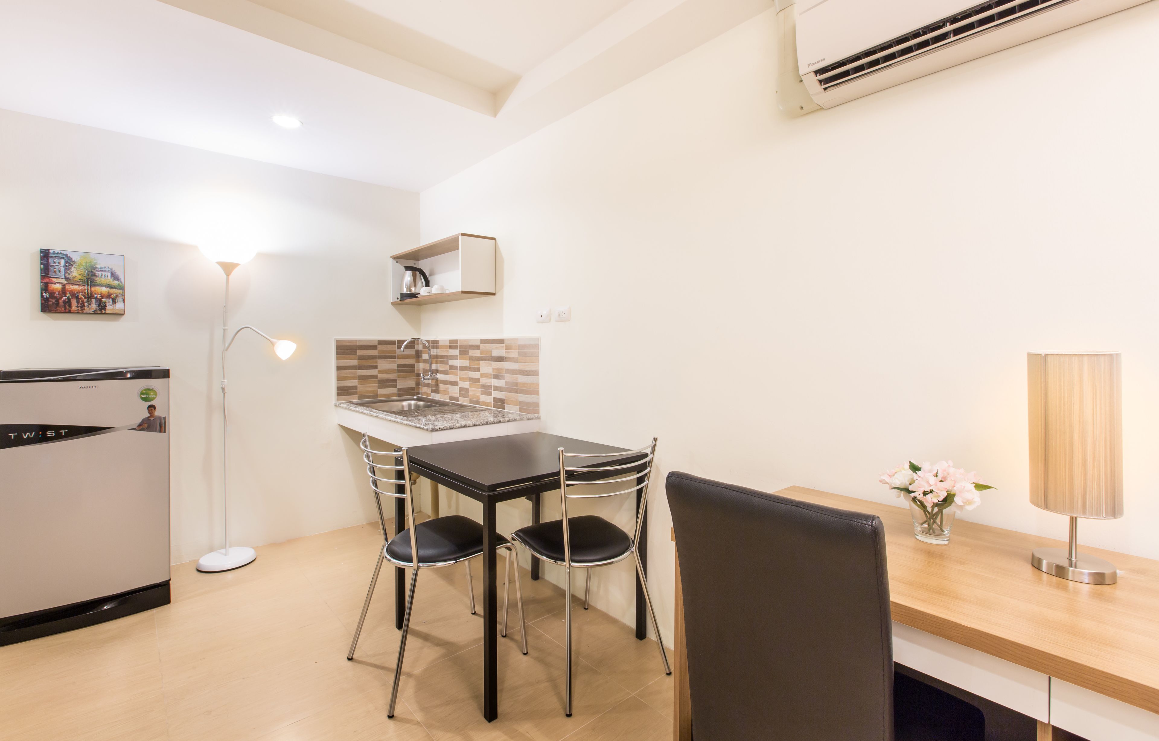 A compact kitchen with a dining area, a refrigerator, a floor lamp, and a small table with chairs.