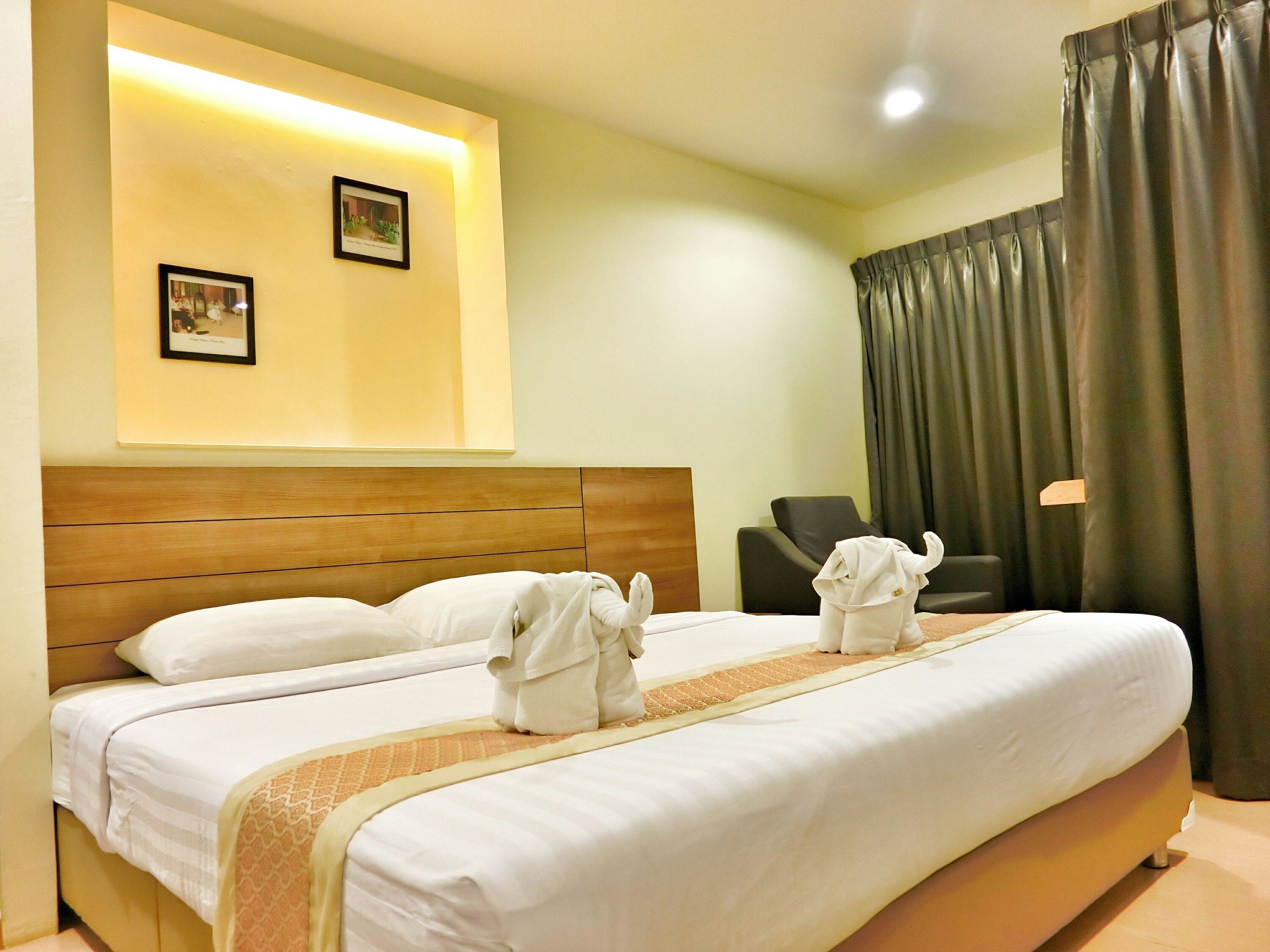 Quarto de hotel com uma cama grande, duas almofadas, cabeceira, uma cadeira, escrivaninha, abajur e cortinas.