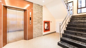 An interior with a modern elevator, a staircase, and a wall-mounted fire extinguisher.