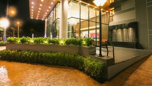 A modern building with a glass facade, outdoor seating area, and a well-lit entrance.