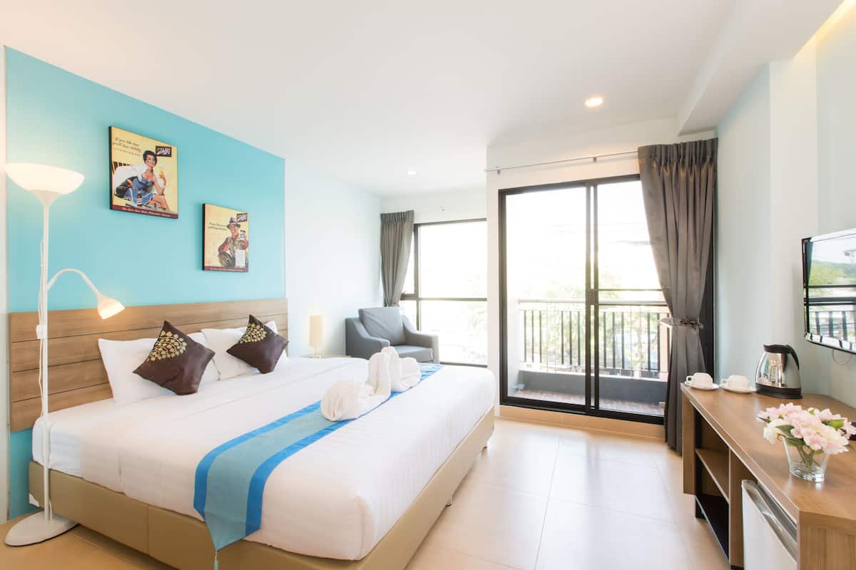 Habitación de hotel con una cama grande, un escritorio con hervidor, una silla y un balcón con cortinas.