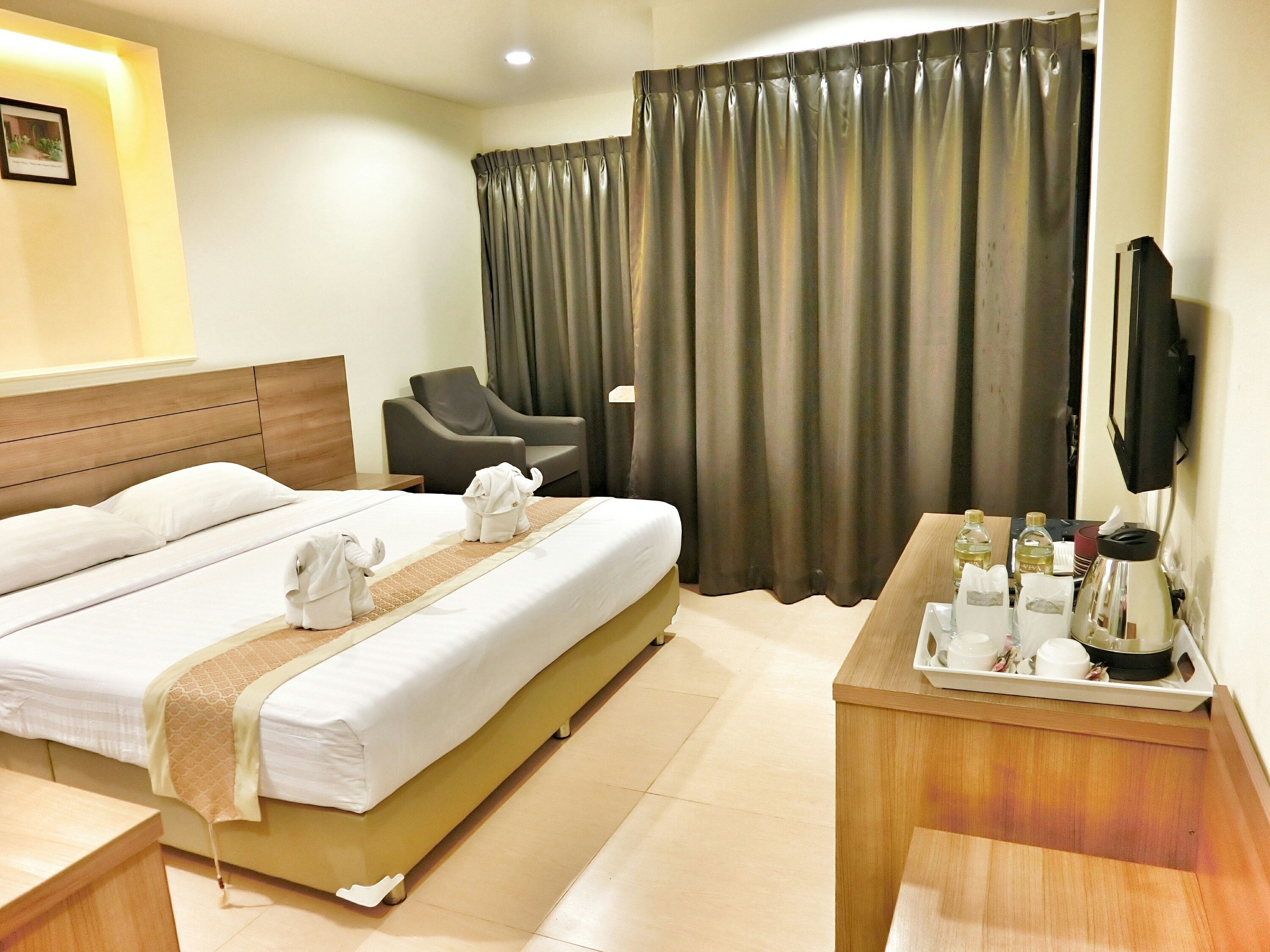 A hotel room with a bed, a chair, a desk with a tray of toiletries, and a television.