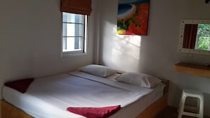 A single bed with white bedding and a red throw, a window with blinds, a painting on the wall, and a small stool.