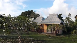A house with a corrugated metal roof, surrounded by lush greenery and palm trees. - Jinta Beach Bungalow (Koh Samui)