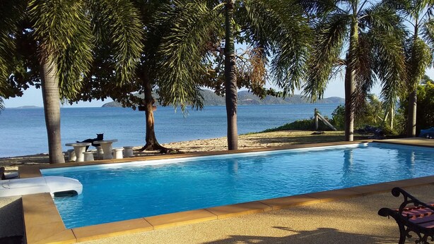 A swimming pool with a view of the sea, surrounded by palm trees and concrete seating. - Jinta Beach Bungalow (Koh Samui)