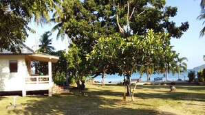 A house with a porch, a grassy yard, and a view of the sea. - Jinta Beach Bungalow (Koh Samui)