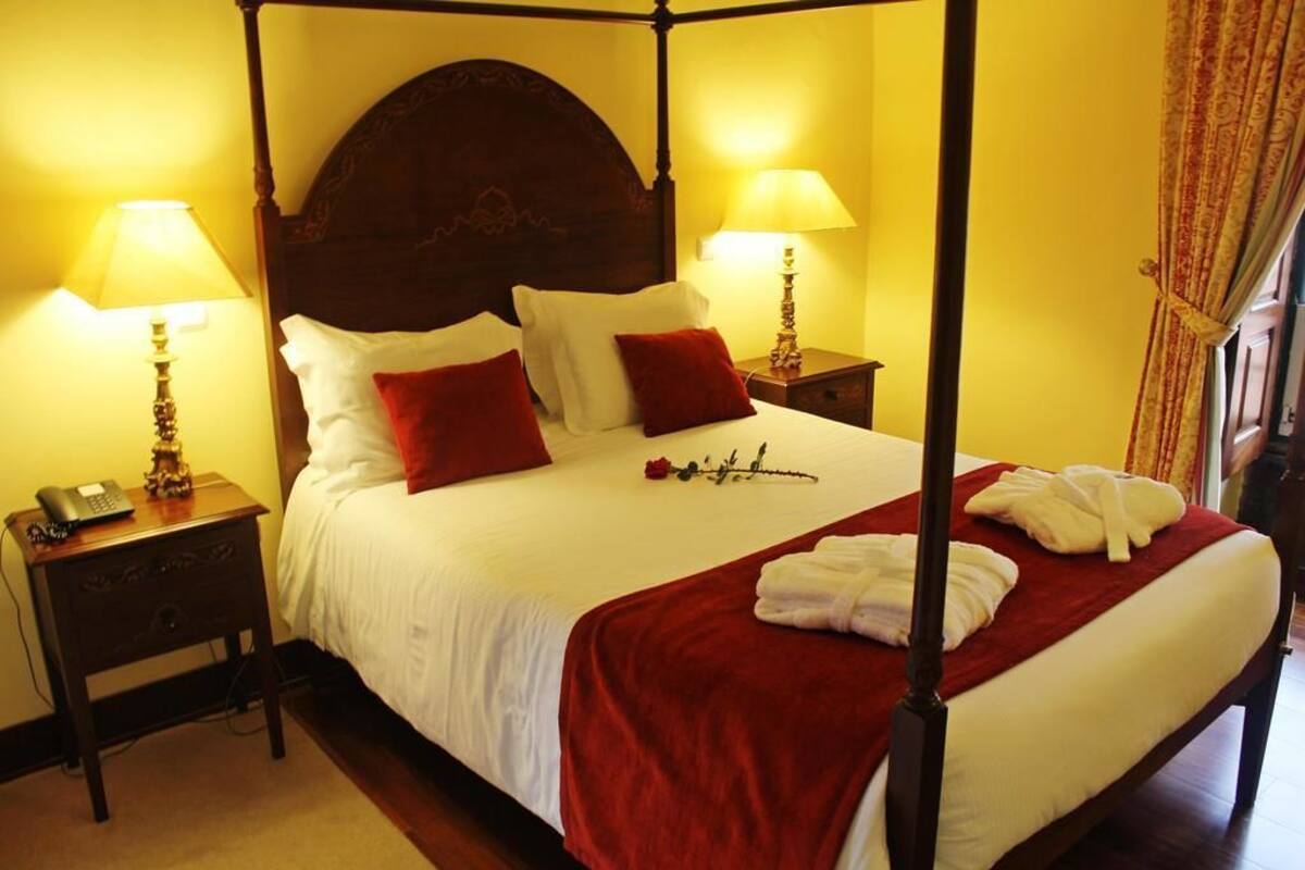A four-poster bed with white linens and red accents, two bedside tables with lamps, and a red throw blanket.