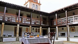 Pátio com mesa posta para o café da manhã, uma torre de sino ao fundo e uma área de estar coberta.
