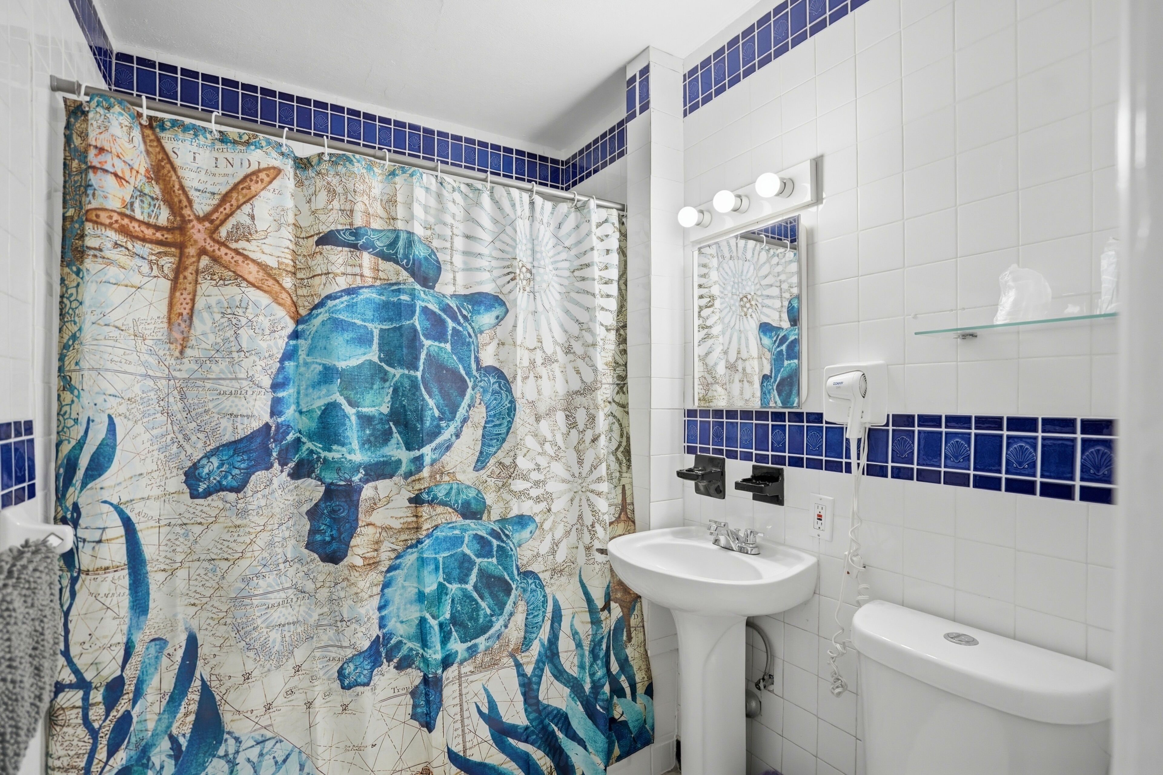 Un bagno con un murale raffigurante un'amato da mare e stelle marine, un lavandino bianco e uno specchio con luci.