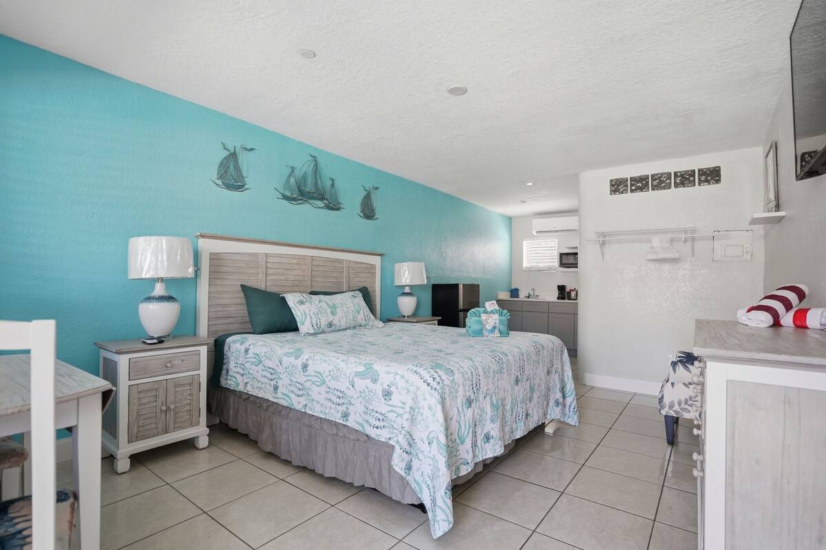 A bedroom with a bed, nightstands, a dresser, and a bathroom visible in the background.