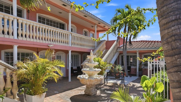 A courtyard with a fountain, palm trees, and a building with balconies and a staircase.