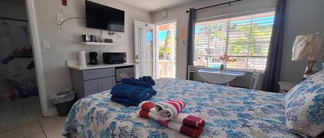 Habitación de hotel con cama, televisor, escritorio con microondas, una mesita y ventana con vistas a zonas verdes.