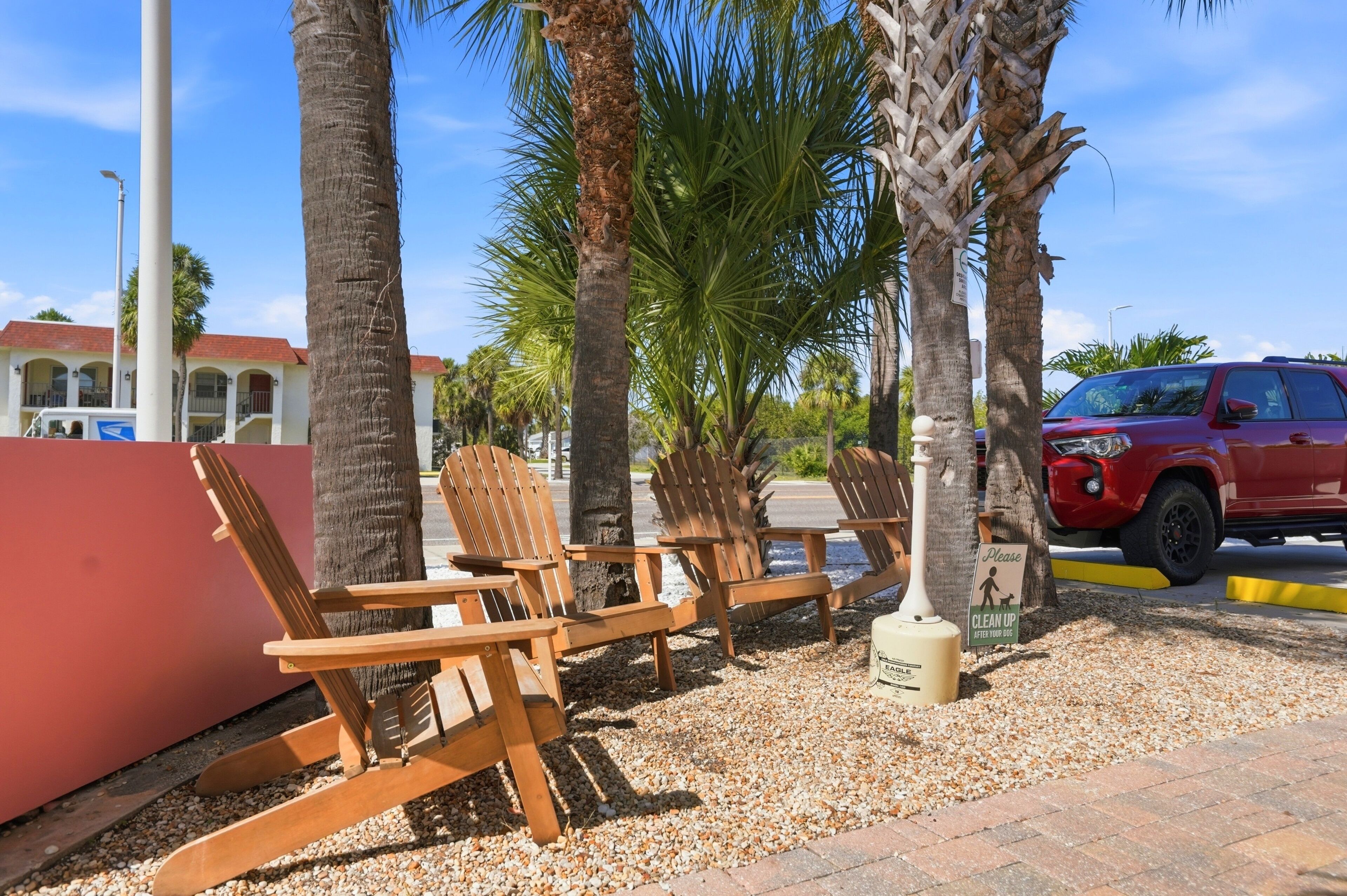 Outdoor seating with wooden chairs and a red vehicle parked nearby.