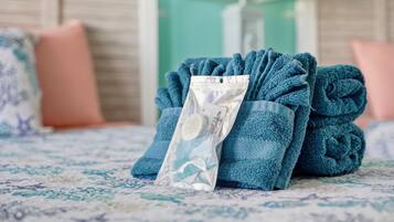 A neatly folded blue towel with a transparent plastic bag containing a bar of soap on a patterned bedspread.