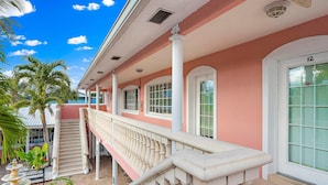 A pink building with a white balcony railing, a staircase, and a palm tree.