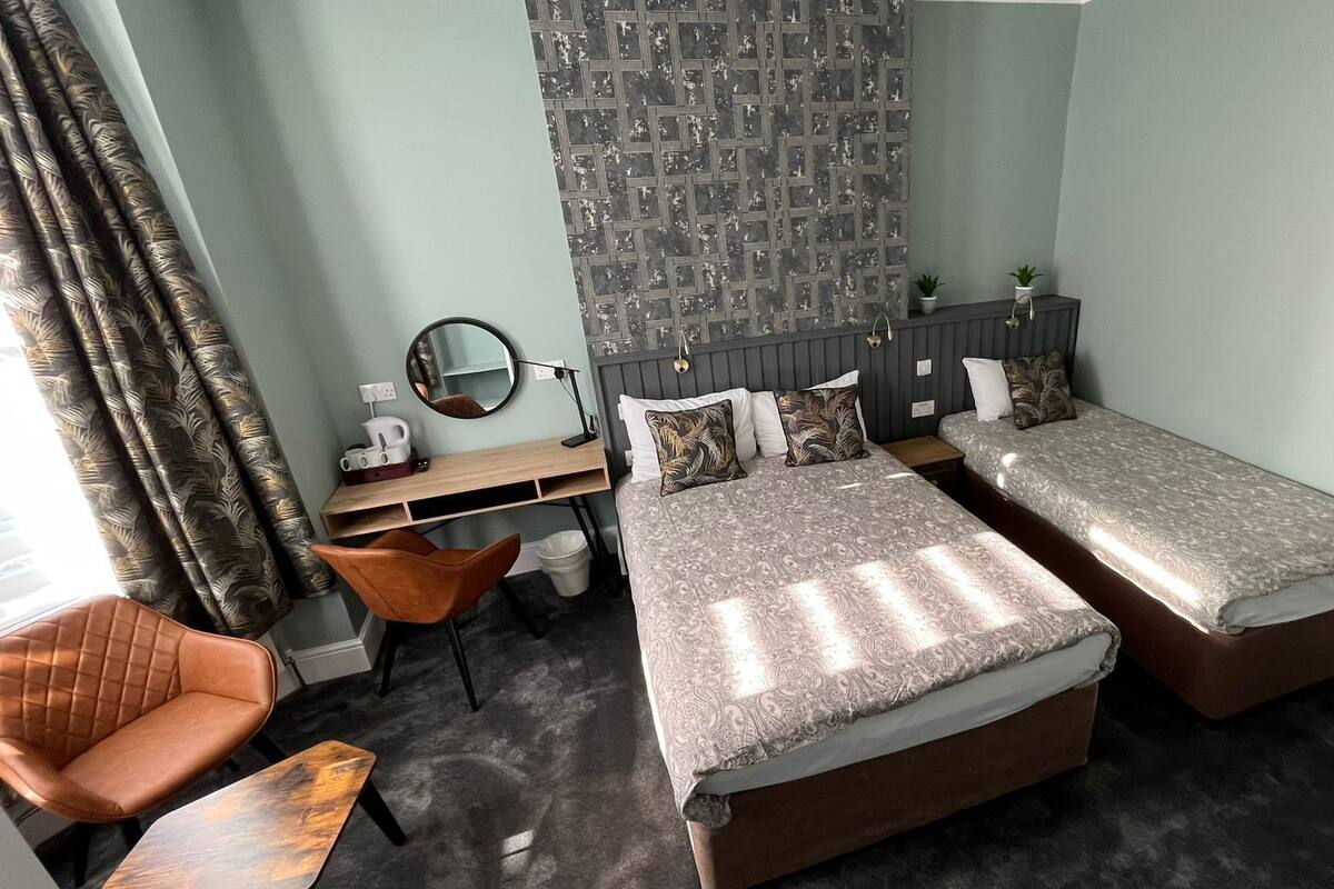 A hotel room with two beds, a desk, a chair, a mirror, and a patterned wall.