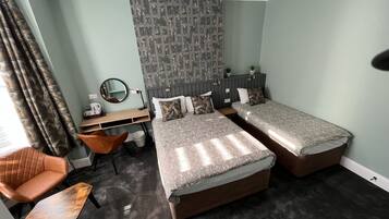 Habitación de hotel con dos camas, un escritorio, una silla, un espejo y un papel tapiz estampado.