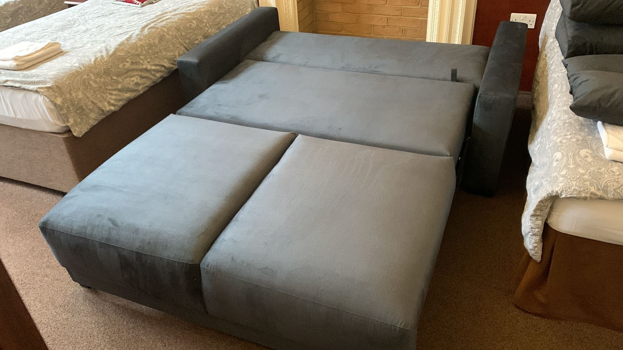 A room with a grey sofa bed, a small table, and a patterned bedspread.