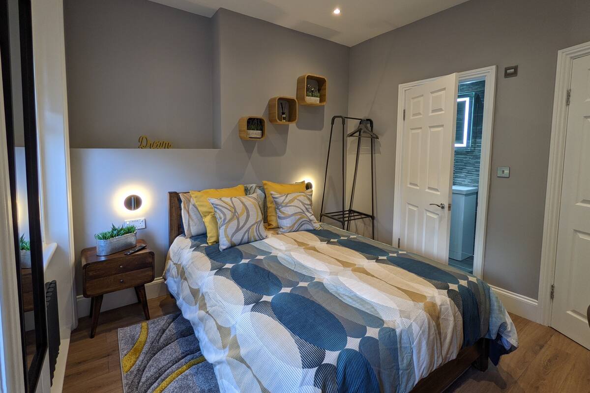 A bedroom with a bed, bedside table, and a wall-mounted shelf with decorative items.