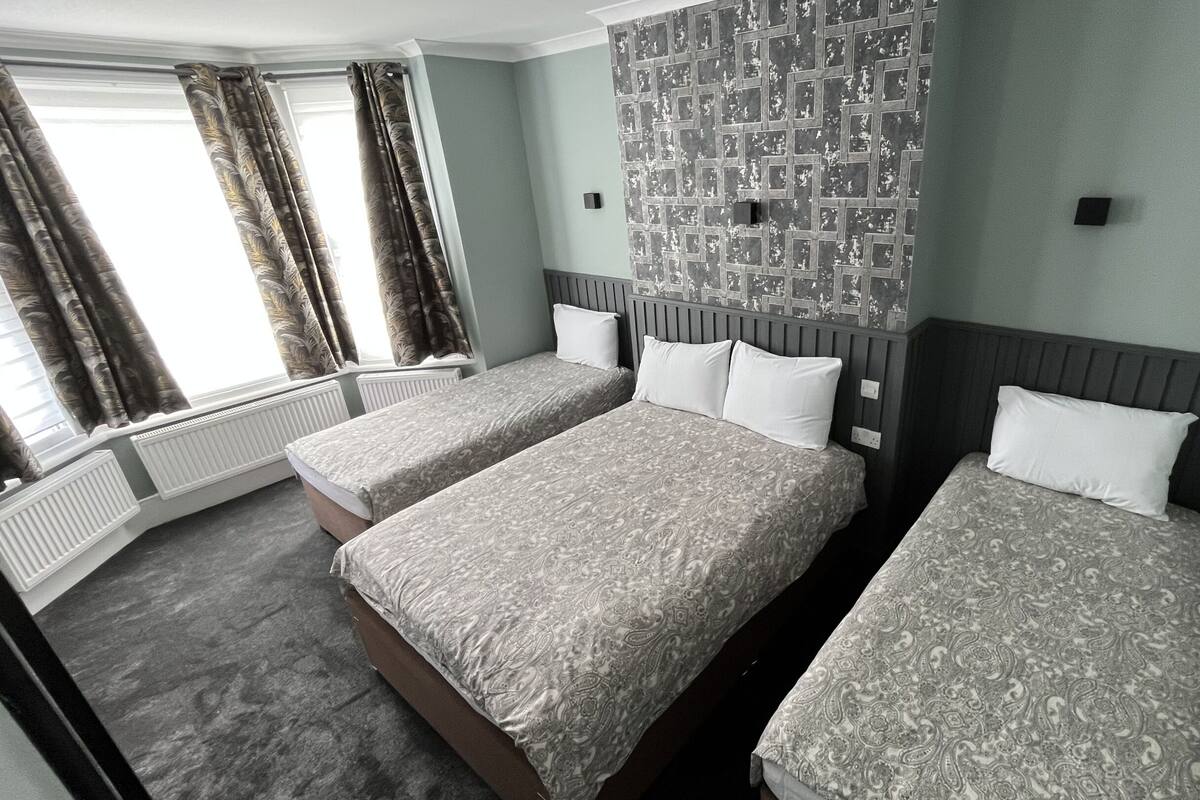 A hotel room with two beds, a patterned wall, and a window with curtains.