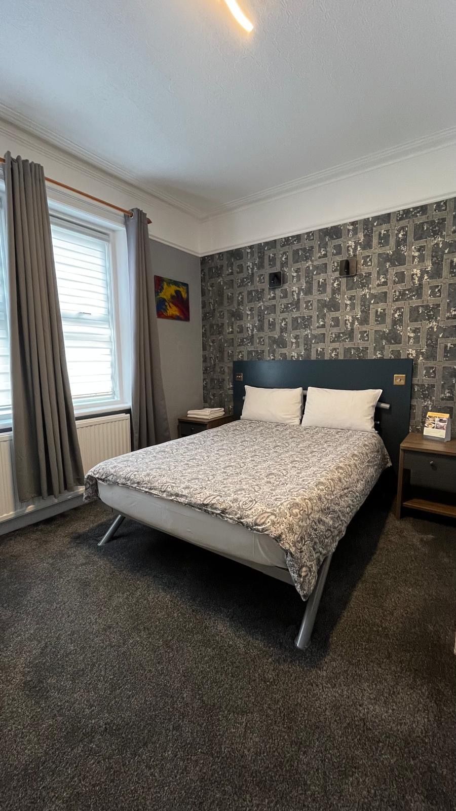 A neatly arranged bedroom with a bed, a nightstand, a radiator, and a window with curtains.