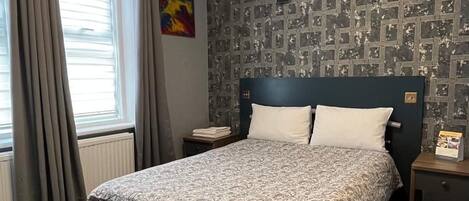 A neatly arranged bedroom with a bed, a nightstand, a radiator, and a window with curtains.