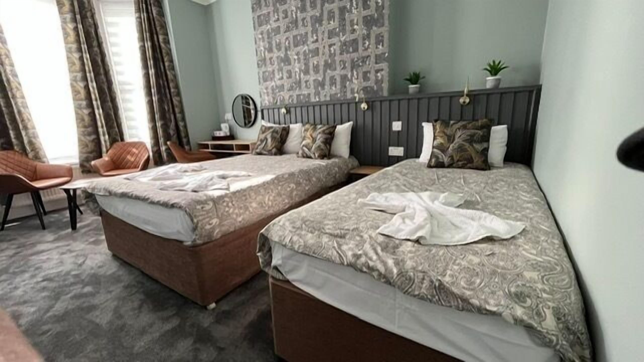 A hotel room with two beds, a desk, a chair, and a wall with patterned wallpaper.