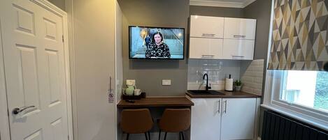 A compact kitchen with a built-in TV, a small dining area, and a window with a geometric pattern.