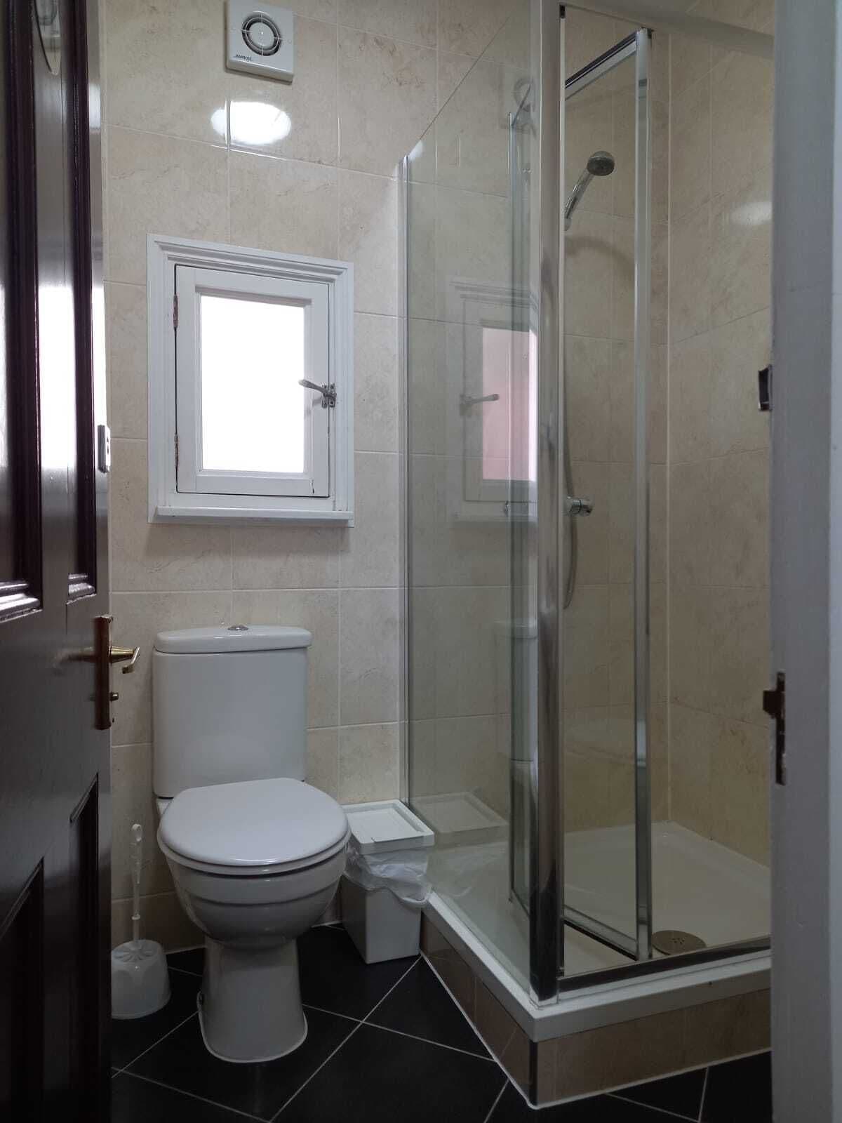 A bathroom with a toilet, a glass-enclosed shower, and a window above the toilet.