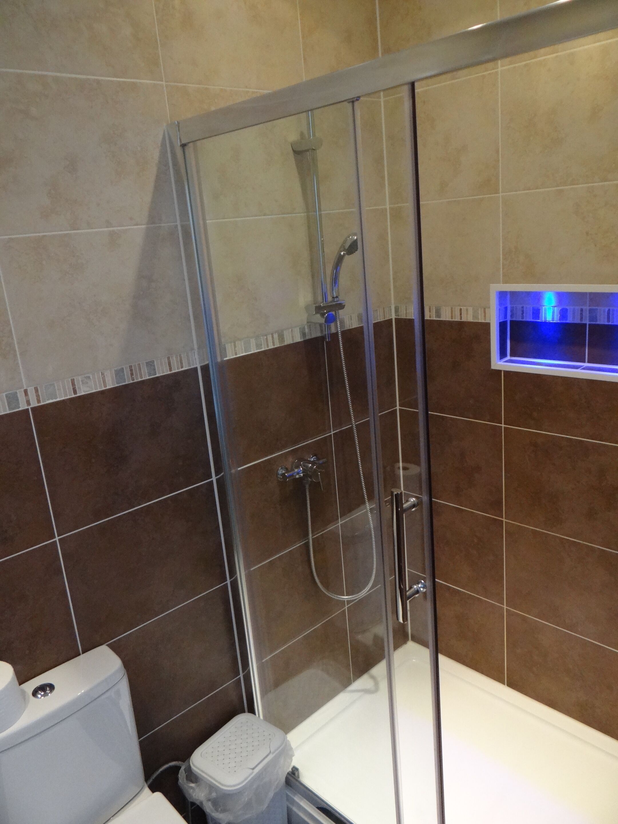 A shower enclosure with a glass door, a handheld showerhead, and a wall-mounted faucet.