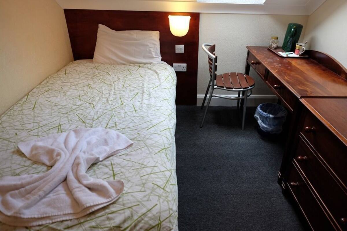 A small, neatly arranged bedroom with a bed, a chair, a desk, and a dresser.