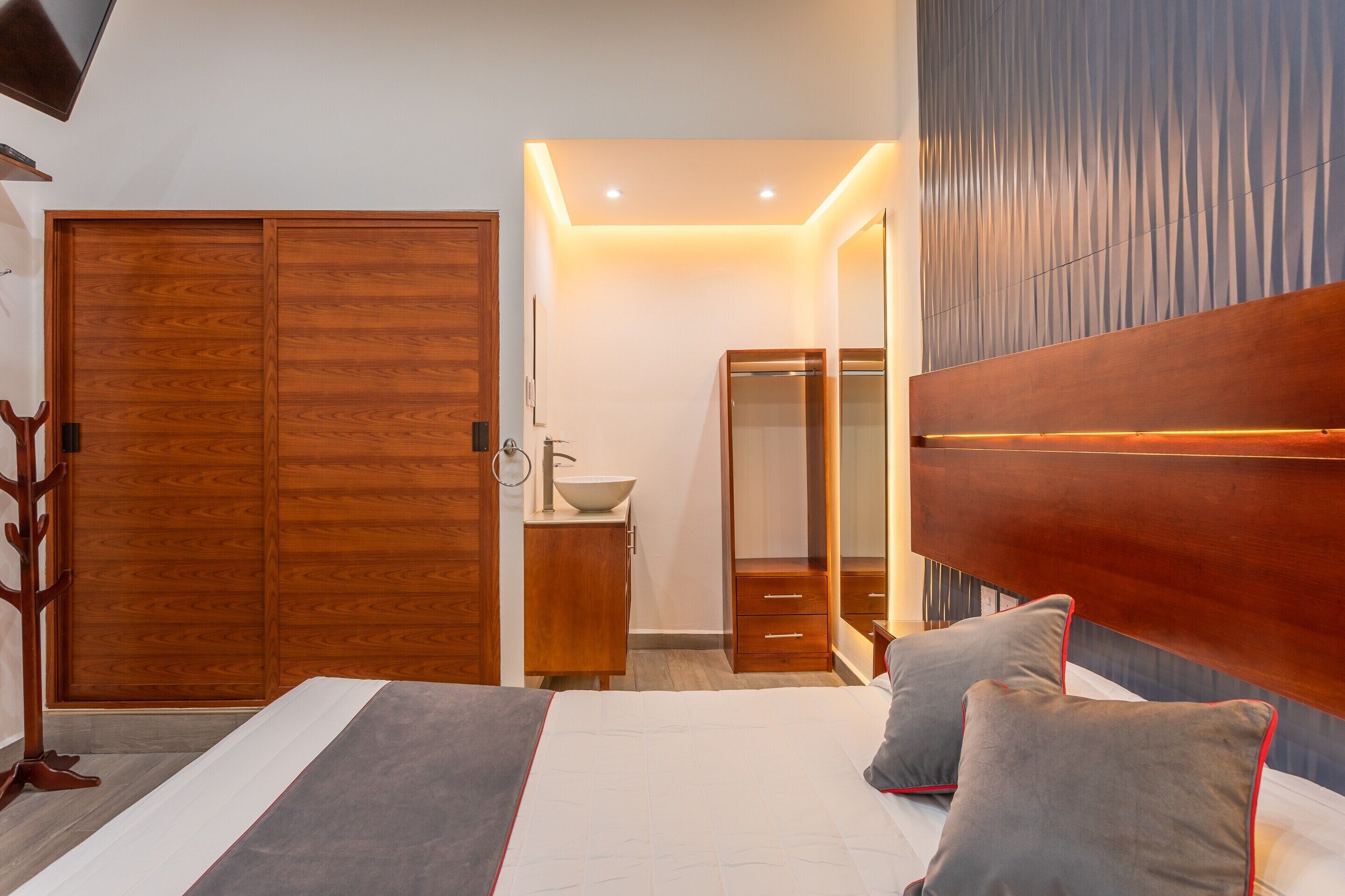 Quarto com uma cama grande, guarda-roupa de madeira, mesa de cabeceira e espelho.