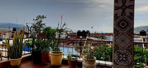 A balcony with potted plants, a view of a cityscape, and a distant mountain range.