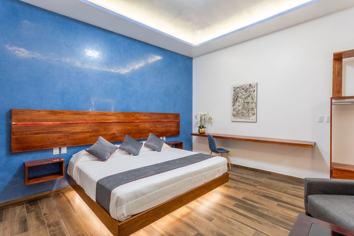 A modern bedroom with a large bed, wooden headboard, bedside tables, a desk, and a chair.
