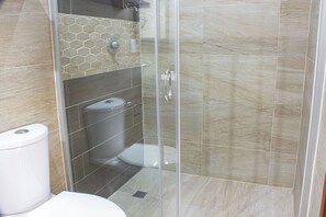 A bathroom with a toilet, a shower with glass doors, and a tiled wall. - Hotel Dos Lunas - Hostel (Oaxaca)