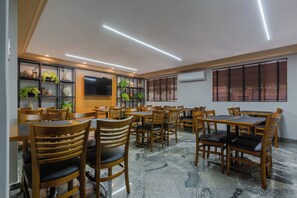A restaurant with multiple tables and chairs, a flat-screen TV mounted on the wall, and shelves with plants and decorative items. - Nohotel Nova Odessa (Nova Odessa)