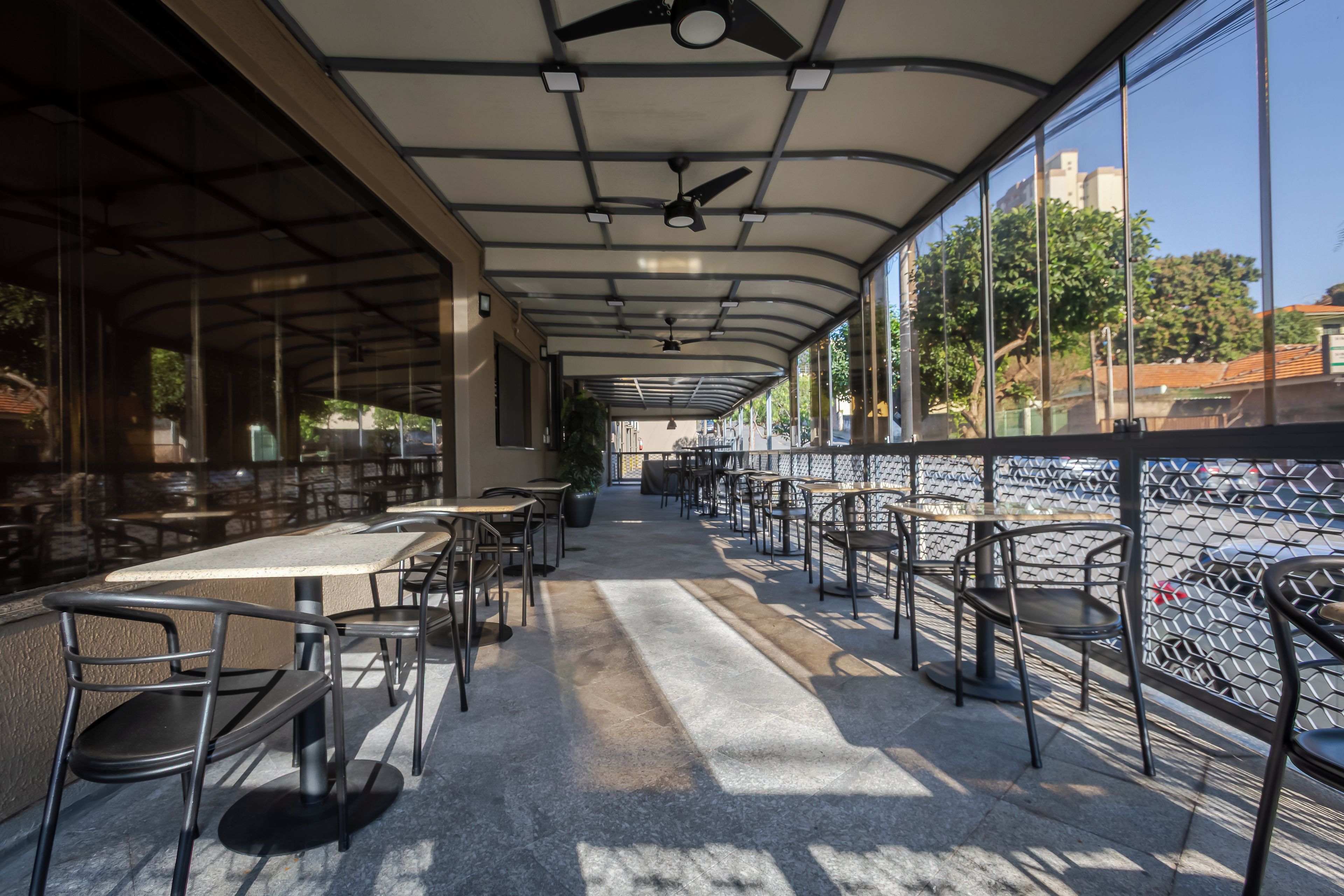Ein Straßencafé mit Tischen und Stühlen, einem Deckenventilator und Blick auf die Stadt durch große Fenster.